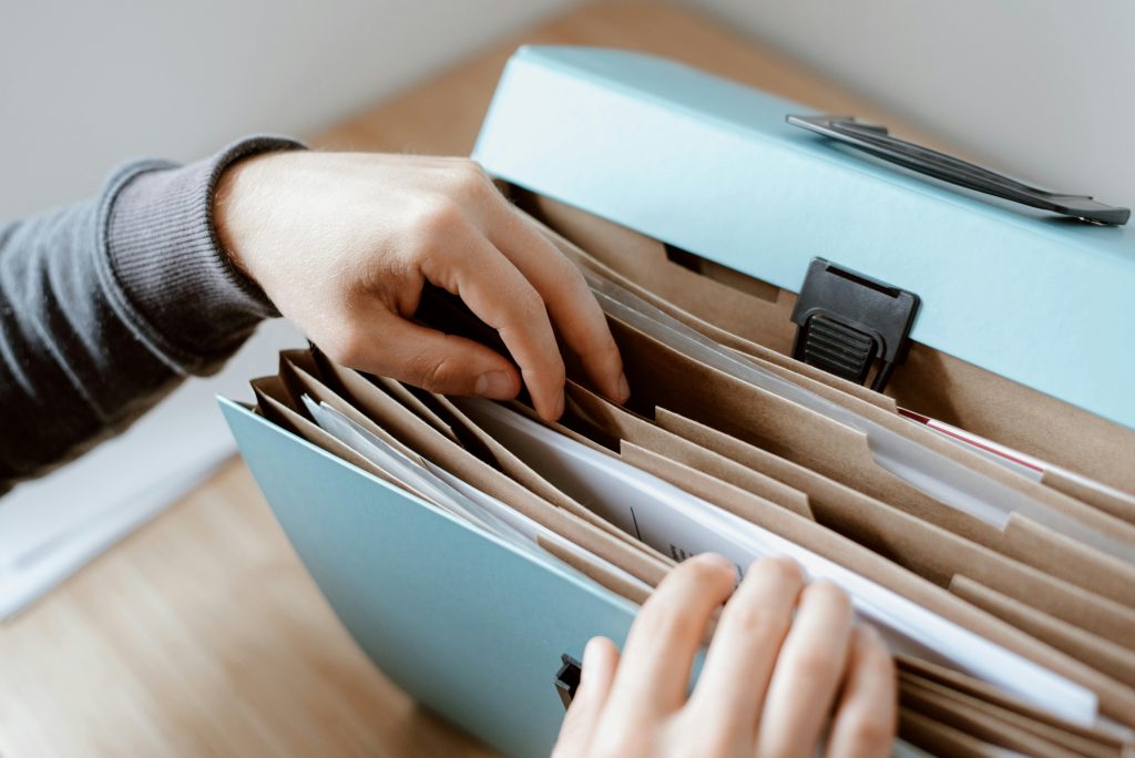 Hands organizing papers in a light-blue file folder on a wooden table.